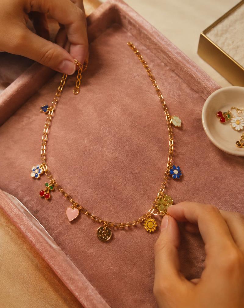 Hands assembling a gold charm necklace on a pink tray